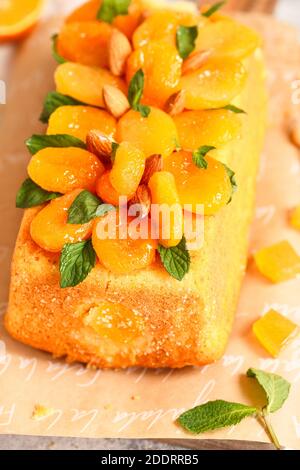 Orange Pound Cake mit frisch gepresstem Orangensaft und Orangenschale, dekoriert mit getrockneten Aprikosen, Minzblättern und Mandeln. Stockfoto