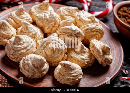 Baiser-Kekse auf einem Teller mit weihnachtszucker-Zuckerrohr, Kaffeetassen, Kaffeebohnen, braunem Zucker und Zimtstangen auf dunklem Holzhintergrund serviert, Stockfoto