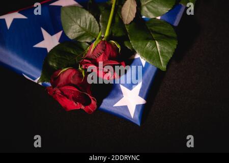 Rote Rosen und amerikanische Flagge auf schwarzem Hintergrund, Bestattungskonzept Stockfoto