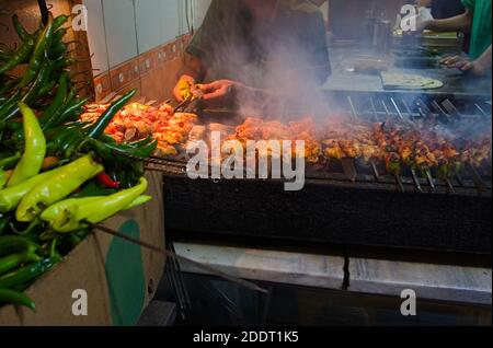 Gegrillter Kebab, türkische Straßengerichte. Hühnerflügel auf der Straße. Hähnchenflügel rösten auf dem Grill im Café auf der Straße. Grüner Chilischote Stockfoto