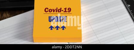 COVID-19 UPDATE-Text auf gelbem Aufkleber auf Desktop-Hintergrund, Bannerformat. Coronavirus-Konzept Stockfoto