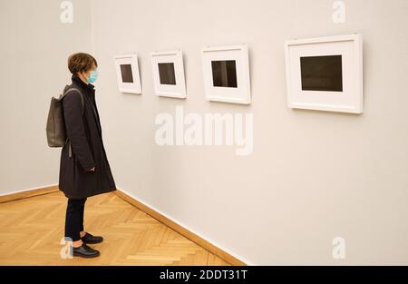 Frau mittleren Alters trägt medizinische Maske und Blick auf Kunstwerke An der Wand in der Ausstellungshalle hängen Stockfoto