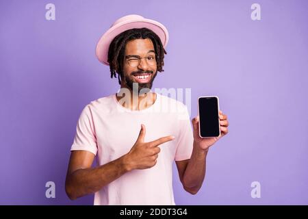 Foto Porträt des Mannes mit Dreadlocks tragen Hut Kopfbedeckung zeigen Finger am Telefon mit Copyspace isoliert auf lebendige lila gefärbt Hintergrund Stockfoto