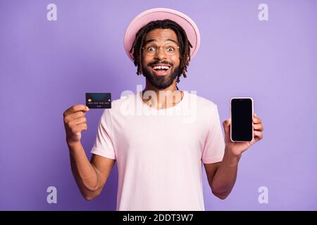 Foto-Porträt von aufgeregt Dreadlocked Kerl in stilvollen Hut Mütze Kopfbedeckung halten Karte und Telefon mit Copyspace isoliert auf Vivid Violett Stockfoto