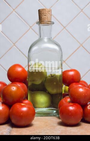 Nahaufnahme von Äpfeln durch die Wirkung von Wasser verzerrt. Dreieckige Zusammensetzung aus Äpfeln, Tomaten und einer Flasche Glas auf der Küchentheke. Stockfoto