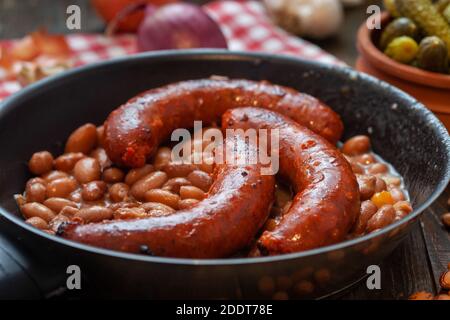 Gebackene Bohnen mit würzigen Schweinswürsten in der Pfanne. Gegrillte Würstchen mit Bohnen. Stockfoto
