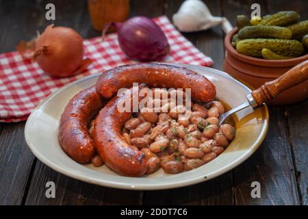 Gebackene Bohnen mit gegrillter Wurst, traditionelle Balkan hausgemachte Mahlzeit. Teller mit würzigen Schweinswürsten und Bohnen. Stockfoto