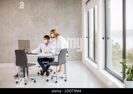 Medical paar Ärzte mit schützenden medizinischen Gesichtsmasken reden und Computer im Offic verwenden Stockfoto