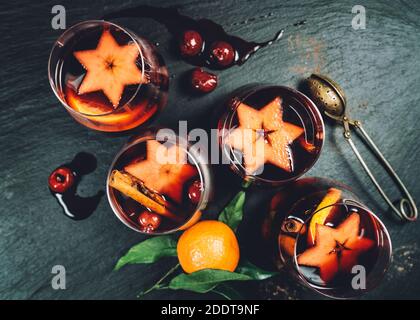 Stillleben von oben mit heißem Glühwein und Gewürzen, Früchten, Zimt serviert in dünnen Glaskrügen auf dem schwarzen strukturierten Steintisch. Weihnachten und New Y Stockfoto