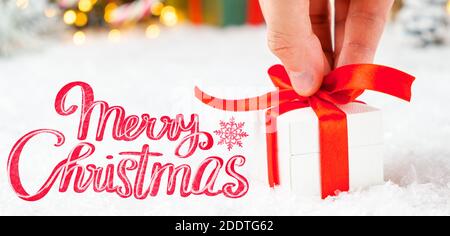 Frohe Weihnachten Grußkarte mit einem Mann Hand hält eine Geschenkbox mit rotem Band auf dem Schnee und verschwommene Lichter auf dem Hintergrund. Stockfoto