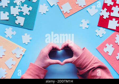 Hände zeigen Herzzeichen. Puzzle-Elemente und mehrfarbige Filzblätter auf blauem Hintergrund. Stockfoto