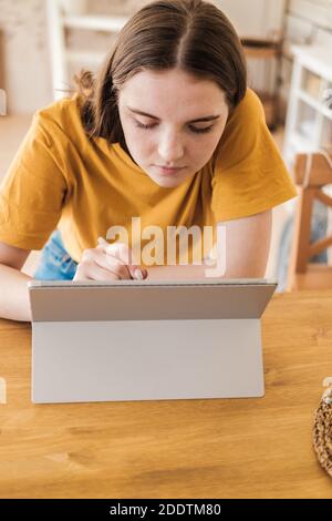 Junge schöne Frau in gelben T-Shirt usimg Tablette für die Arbeit, Online-Geschäft, Studium zu Hause sitzen. Selbstisolation, Studium, Arbeit während der Quarantäne Stockfoto