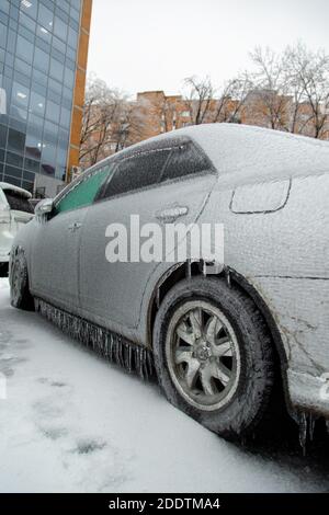 Der graue Pkw war nach dem nassen Regen in der Stadt im Winter mit einer dicken Eiskruste bedeckt. Stockfoto