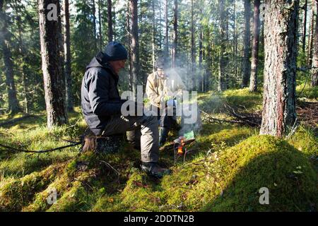 Ein älteres Paar, das sich beim Pilzpflücken ausruhen kann, um ein kleines Lagerfeuer im Wald zu sitzen, Foto aus Nordschweden. Stockfoto