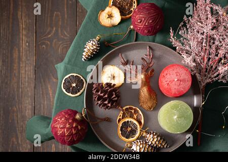 Weihnachtliche Komposition in Burgunder- und Brauntönen, weihnachtsbaumschmuck und Kerzen, Trockenfrüchte und Deko-Hirsche auf einer grünen Tischdecke Stockfoto