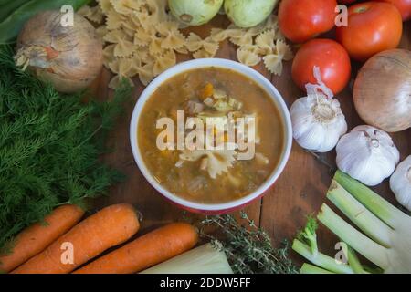 Draufsicht auf eine kochende Minestrone-Suppe, eine typische dicke Gemüsesuppe, ursprünglich aus Italien, serviert in einer Schüssel mit Farfalle Pasta. Stockfoto