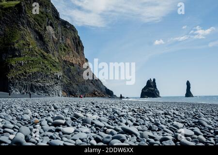 Blick auf die Reynisdrangar Felsformationen vom Reynisfjara Beach mit den schwarzen Kieselsteinen des Strandes im Vordergrund an einem sonnigen Tag. Stockfoto