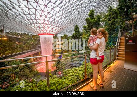 singapur, singapur - 4. März 2020: Junge Mutter hält Kleinkind Mädchen Reisende schaut auf Wasserfall in Jewel Mall in singapur changi International Stockfoto