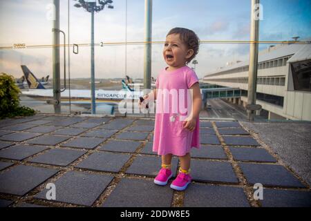 SINGAPUR - 11. FEBRUAR 2020: Ein verängstigtes Kleinkind in einem rosa Kleid weint im Sonnenblumengarten auf dem Dach des Changi Flughafens im Hintergrund Stockfoto