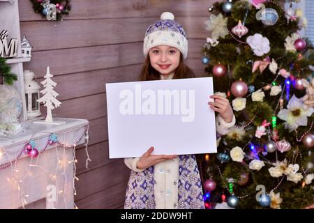 Ein Mädchen in einem Santa Claus Helfer Kostüm. Das Mädchen hält ein leeres Stück Papier und zeigt auf den Kopierraum. Stockfoto