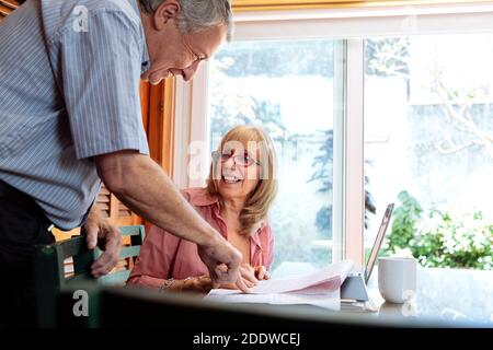 Eine ältere Frau und ein Mann lächeln und reden über Geschäfte. Die Frau ist ein Tisch mit einem Laptop vor ihr. Klares, helles Bild. Stockfoto