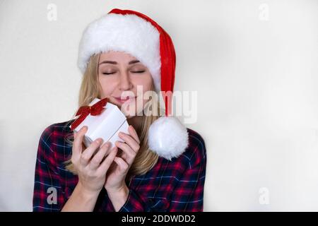 Weihnachtsgeschenk. Junge kaukasische Frau mit Geschenk in ihren Händen lächelt und genießt es, ihre Augen vor einem weißen Hintergrund zu schließen Stockfoto