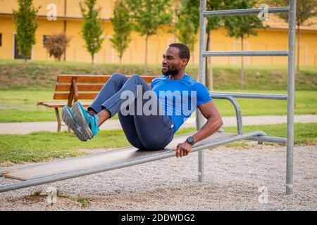 Fitness afro american boy doing situps Outdoor - schöner afrikanischer Mann macht Stretching-Übungen im Open-Air-Fitness-Studio im Park. Bauchmuskeln Übungen auf der Stockfoto