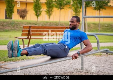 Fitness afro american boy doing situps Outdoor - schöner afrikanischer Mann macht Stretching-Übungen im Open-Air-Fitness-Studio im Park. Bauchmuskeln Übungen auf der Stockfoto