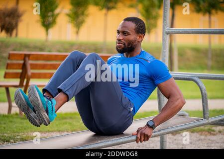 Fitness afro american boy doing situps Outdoor - schöner afrikanischer Mann macht Stretching-Übungen im Open-Air-Fitness-Studio im Park. Bauchmuskeln Übungen auf der Stockfoto