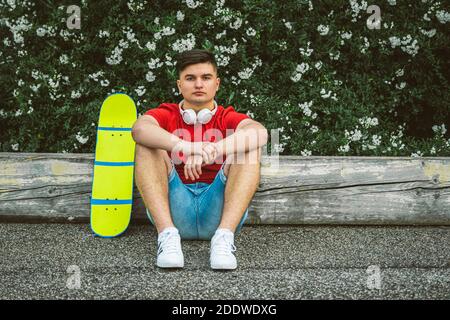 Teen Boy ist sitzend ruht mit Longboard - Junge Erwachsene Outdoor-Skaten - EIN junger Mann sitzt mit einem Longboard - Portrait des schönen Jungen Skater Stockfoto