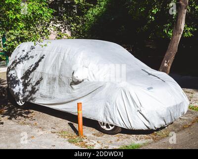 Das Auto bedeckt mit einem Deckstand im Innenhof unter Die vom Sonnenlicht beleuchteten Bäume Stockfoto