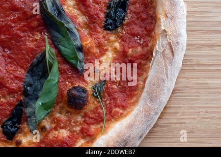 Schuss einer veganen, käsefreien Marinara-Pizza mit Basilikum Blätter auf einem rustikalen Holzbrett Stockfoto