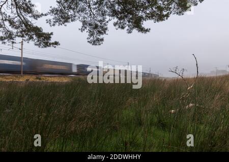 Intermodaler Containerfrachtzug durch den Nebel auf der zu beschleunigen west Coast Mainline in Cumbria mit Bewegungsunschärfe Stockfoto