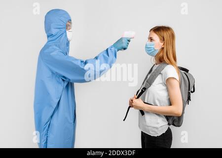 Arzt trägt Schutzanzug, medizinische Maske mit Brille und Handschuhe, verwendet Infrarot-Stirn-Thermometer, um Körpertemperatur auf Symptome von COV zu überprüfen Stockfoto