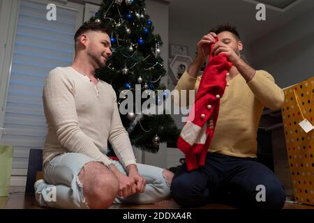 Junge Gay Paar mit Spaß feiern Weihnachten und Neujahr. Vor dem Christmassenbaum sitzen und Geschenke öffnen. Hochwertige Fotos Stockfoto