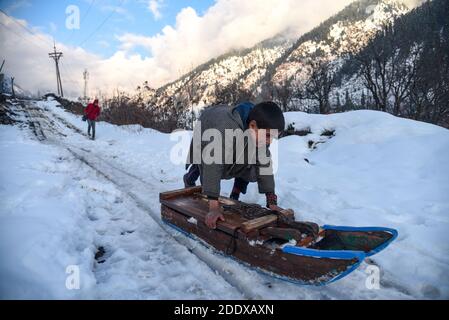 Ganderbal, Indien. November 2020. Ein Baqarwal Junge spielt mit Schneeschlitten außerhalb seines Hauses nach einem Schneefall in Ganderbal Kaschmir.Wetter verbessert sich in Kaschmir Indien nach 3 Tagen, Tag Temperatur steigt, während Nacht Temperatur weiter zu tauchen. Kredit: SOPA Images Limited/Alamy Live Nachrichten Stockfoto