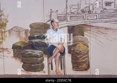 Ein Wandgemälde an der Ong Ang Walking Street entlang Klong Ong und in der Chinatown / Phahurat Gegend von Bangkok, Thailand, zeigt Händler sitzen zwischen seinen Waren Stockfoto