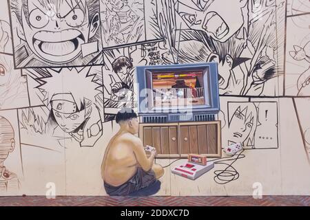 Ein Wandgemälde in der Ong Ang Walking Street entlang Klong Ong und in der Chinatown / Phahurat Gegend von Bangkok, Thailand, zeigt einen Jungen mit seiner Spielkonsole Stockfoto