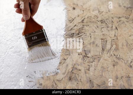 Pinsel mit weißer Farbe in Handfarben Holzfläche von Hauswand Stockfoto