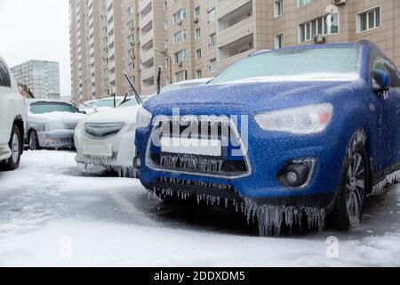 Der blaue SUV und andere Autos stehen in der Stadt gefroren und eisig vom Regen im Winter. Durch Eis blockiert. Stockfoto