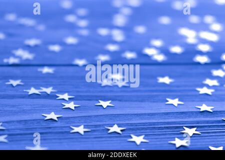 Festlicher kreativer Hintergrund mit funkelnden Konfetti in Form von Sternen auf blauer Kulisse. Urlaubskonzept. Selektiver Fokus. Nahaufnahme. Speicherplatz kopieren. Stockfoto
