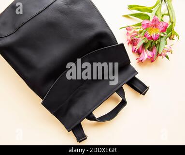 Damen Leder schwarzen Rucksack und Blumen auf einem hellgelben Hintergrund Stockfoto