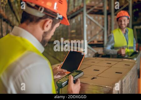 Zwei Lagerarbeiter in Helmen, die Waren kontrollieren Stockfoto