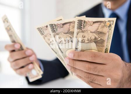 Geschäftsmann Zählen Geld Berechnung der Umrechnungskurs der japanischen Yen Banknote Währung in seinen Händen Stockfoto