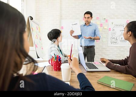 Asiatische männliche Lehrer zeigen und erklären Beispiel auf Papier zu Gruppe von Studenten im Klassenzimmer Stockfoto