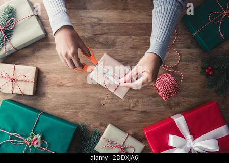 Frau Band Schnur um Geschenkbox nach dem Einwickeln mit Papier auf Holztisch, Vorbereitung für Weihnachten feiern Stockfoto