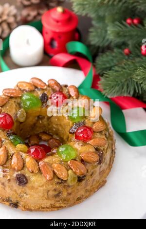 Glasierte runde hohle bunte Weihnachten Obstkuchen gekrönt mit Mandeln und glace Kirschen auf weißem Teller mit grünen Kiefernnadeln und Bändchenverzierungen Stockfoto