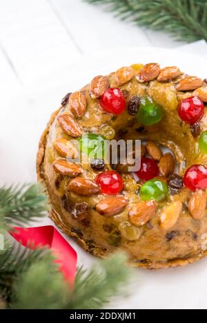 Glasierte runde hohle bunte Weihnachten Obstkuchen gekrönt mit Mandeln und glace Kirschen auf weißem Teller mit grünen Kiefernnadeln und Bändchenverzierungen Stockfoto