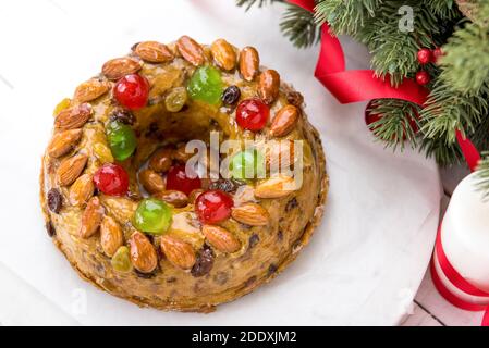 Glasierte runde hohle bunte Weihnachten Obstkuchen gekrönt mit Mandeln und glace Kirschen auf weißem Teller mit grünen Kiefernnadeln und Rote Schleife decorati Stockfoto