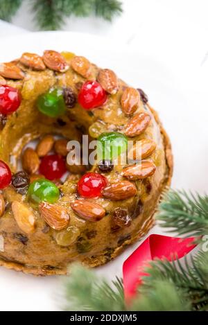 Glasierte runde hohle bunte Weihnachten Obstkuchen gekrönt mit Mandeln und glace Kirschen auf weißem Teller mit grünen Kiefernnadeln und Rote Schleife decorati Stockfoto